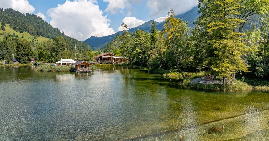 Forellensee mit Veranstaltungsbereichen am Ufer und Bergen im Hintergrund