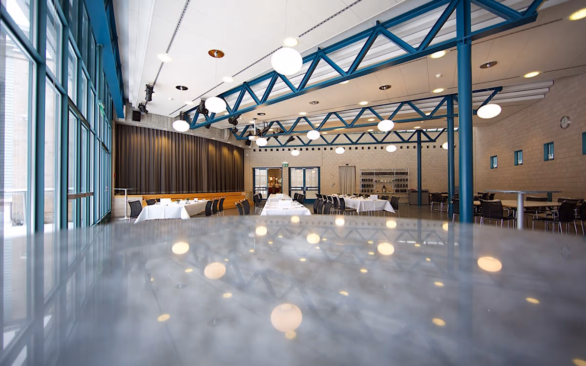 Saal mit Bühne, grossen Fenstern und gedeckten Tischen