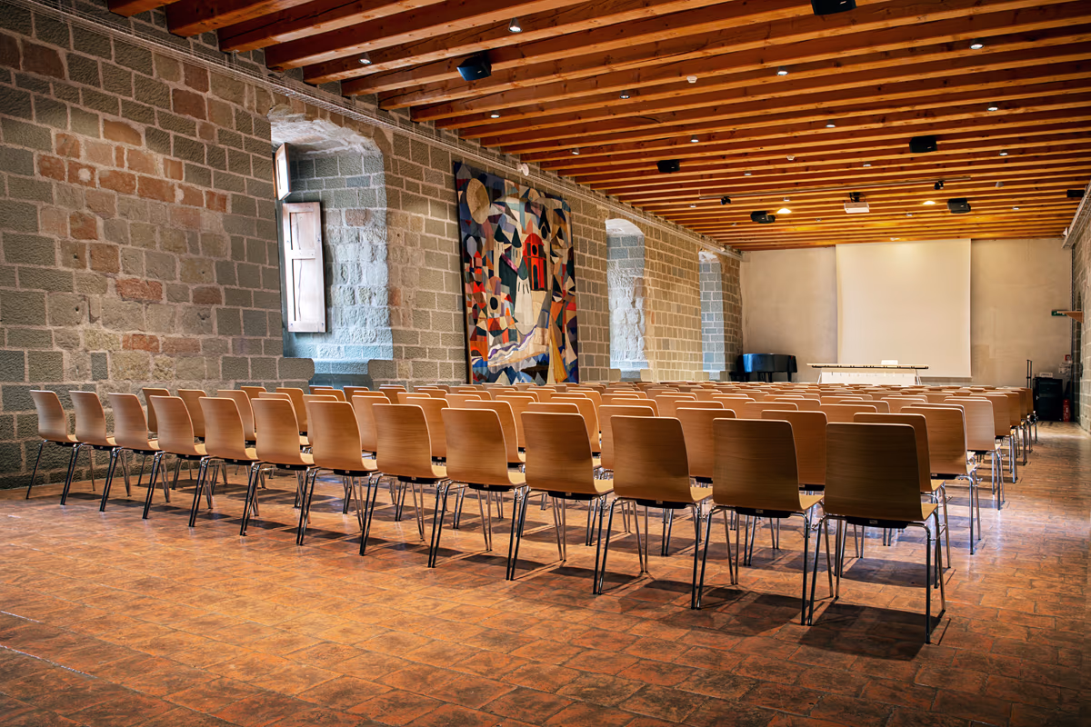 Aula Magna im Château d’Yverdon-les-Bains mit Stuhlreihen, Steinwänden und Holzbalkendecke